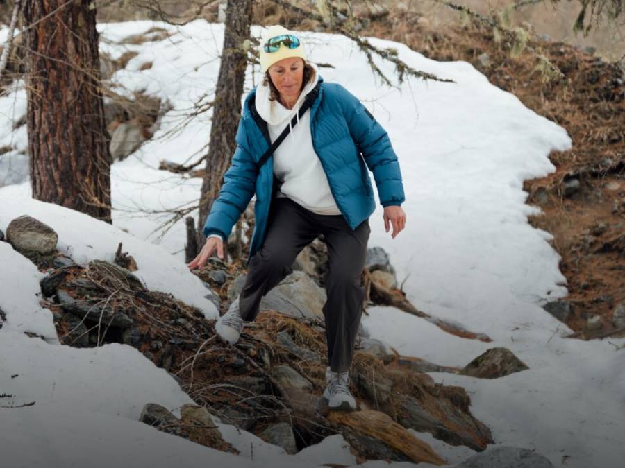 Zwei Schlitten mit je zwei Personen fahren eine verschneite Piste hinunter. Die Personen lachen und tragen Winterkleidung, Mützen und Sonnenbrillen; im Hintergrund schneebedeckte Berge.