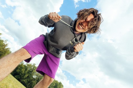 Frau mit lockigem Haar und einem orangen T-Shirt hockt auf einem Felsen vor einer bergigen&nbsp;Landschaft.