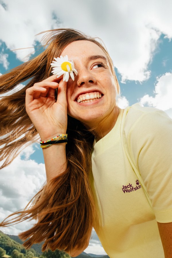 Junger Mann hält eine Sonnenbrille in der Hand und schaut nachdenklich zur Seite vor einer sonnigen Landschaft.