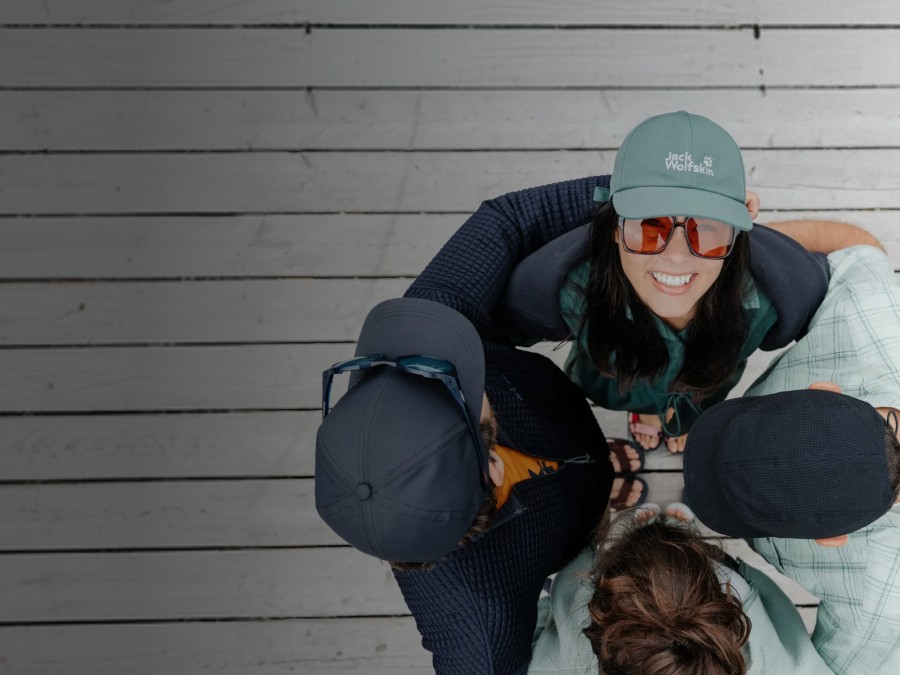 Zwei Schlitten mit je zwei Personen fahren eine verschneite Piste hinunter. Die Personen lachen und tragen Winterkleidung, Mützen und Sonnenbrillen; im Hintergrund schneebedeckte&nbsp;Berge.