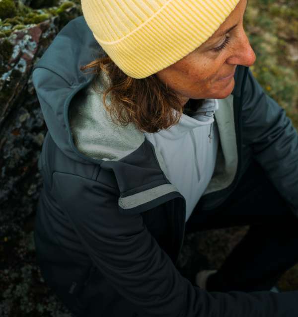 Dame in Jacke und Fleece rastet an einem Felsstein